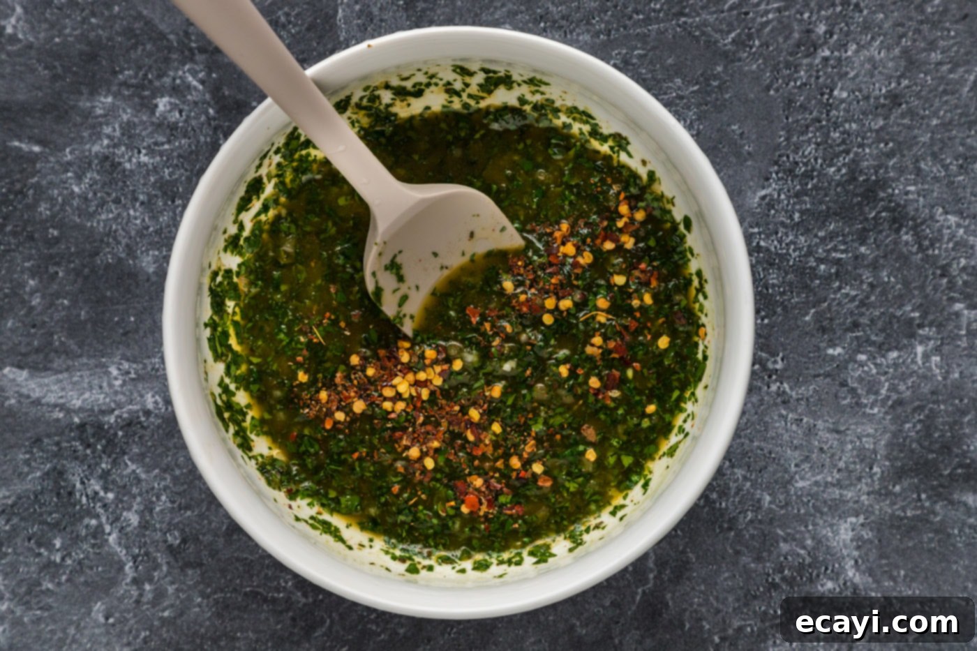 Chimichurri Sauce 7 chimichurri sauce in a mixing bowl with red pepper flakes being stirred in