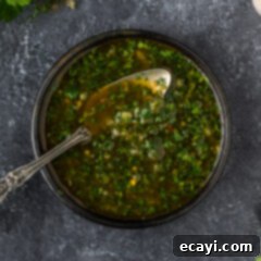 Chimichurri Sauce 9 Close up photo of a bowl of Chimichurri with a spoon in it, showcasing vibrant green