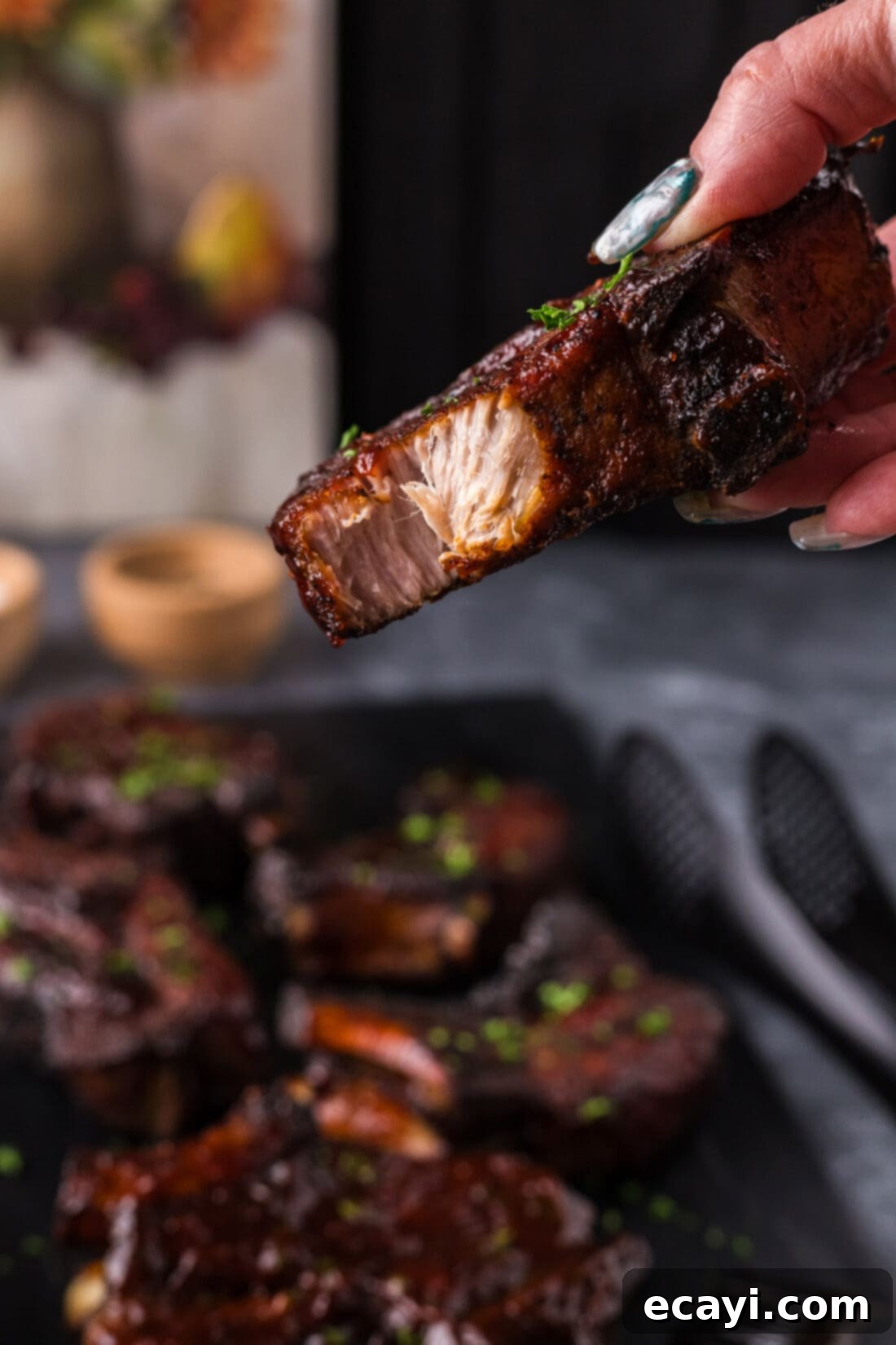 Down-Home Country Ribs 12 A hand holding up a perfectly cooked Country Style Rib with a bite taken out, showing its tenderness.
