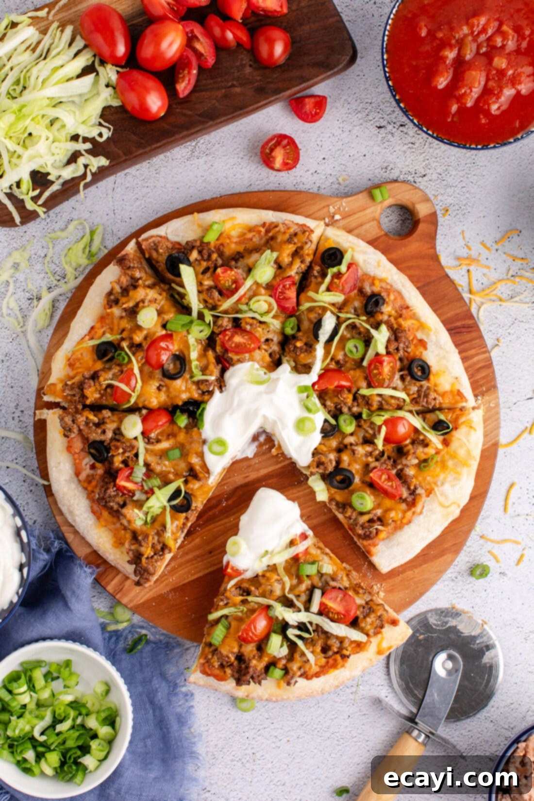 Fiesta Taco Pizza 2 Overhead photo of a delicious Taco Pizza cut into slices, topped with fresh ingredients like lettuce, tomatoes, and sour cream.