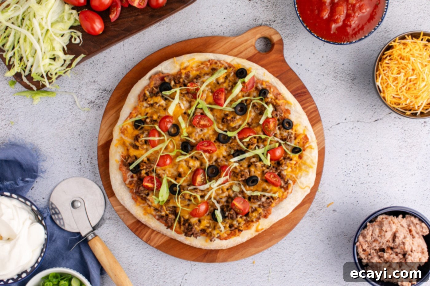 Fiesta Taco Pizza 9 Easy baked taco pizza on a serving board, garnished with fresh lettuce, sour cream, and green onions.