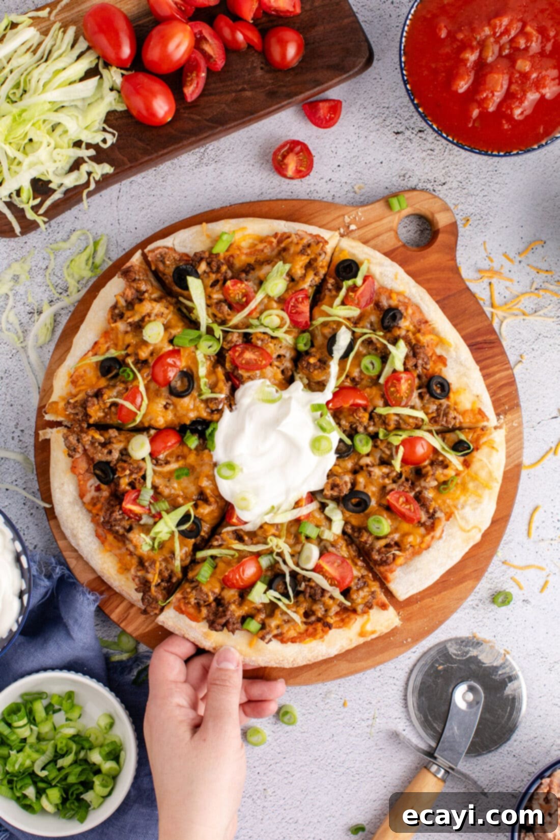Fiesta Taco Pizza 10 A hand reaching for a slice of freshly baked Taco Pizza, garnished with vibrant toppings.