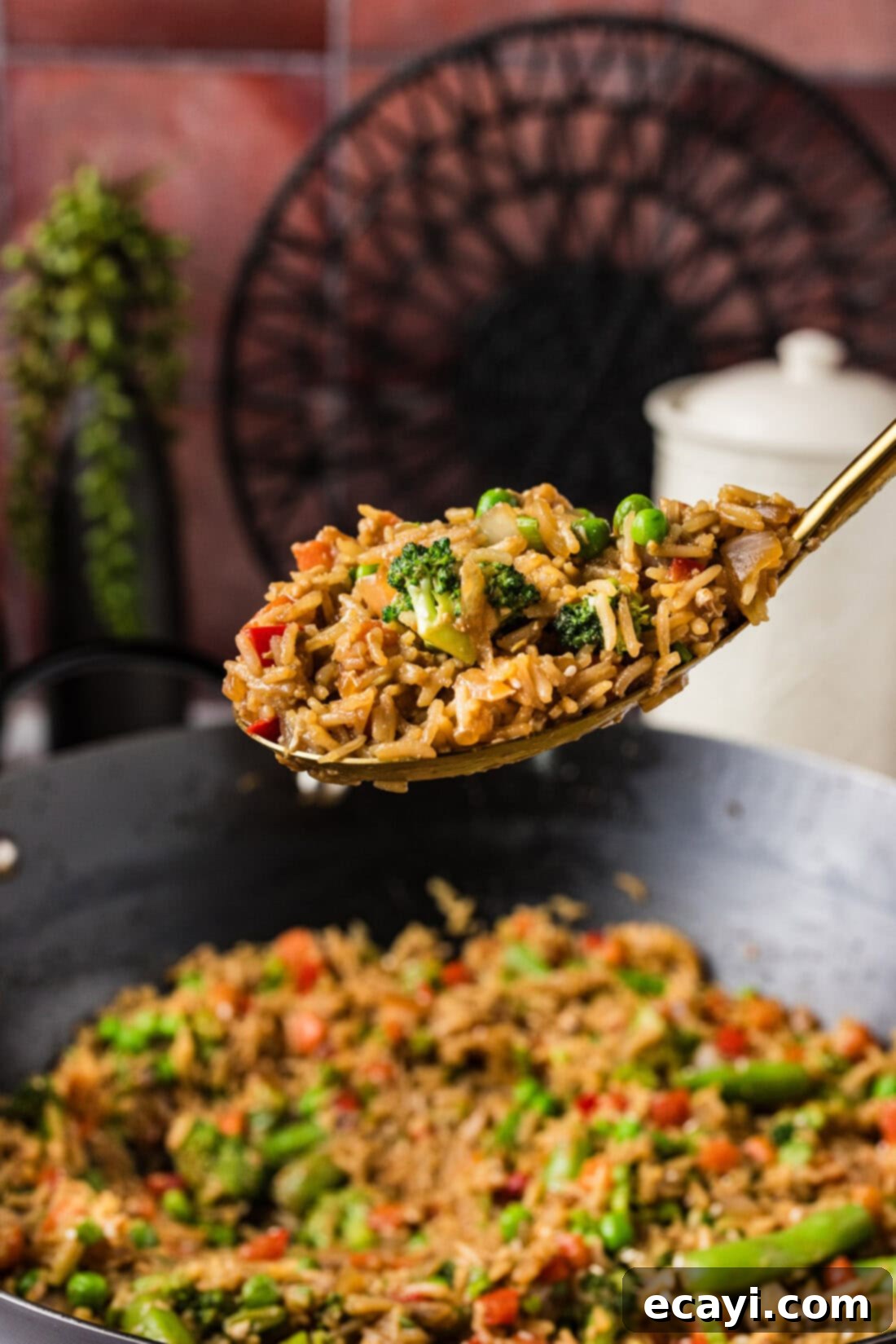Garden Medley Fried Rice 3 Spoonful of golden Vegetable Fried Rice held above a large wok filled with more rice and colorful stir-fried vegetables.