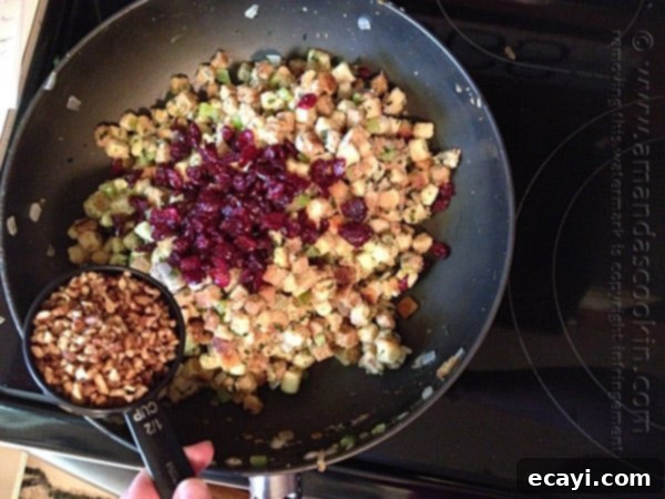 Aromatic Herb Stuffing 8 A photo of dried cranberries and pecans being added to the skillet of stuffing.
