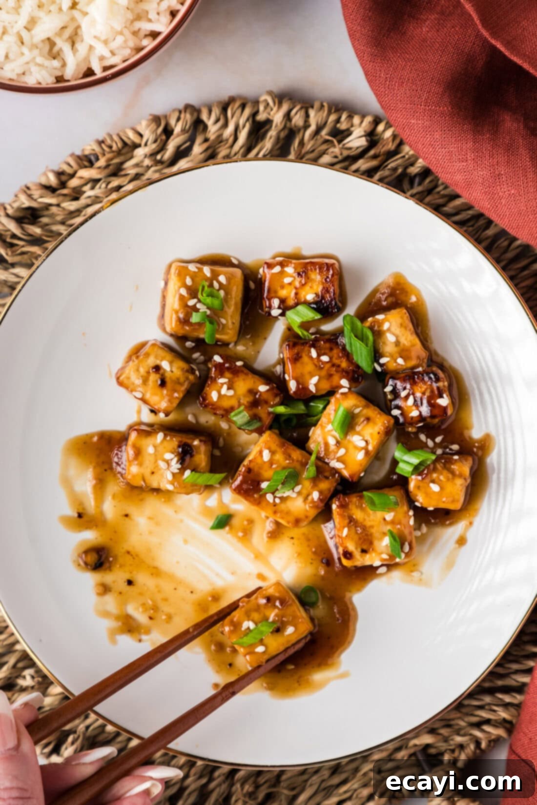 Sticky Honey Garlic Tofu 3 Chopsticks grabbing a piece of Honey Garlic Tofu on a plate