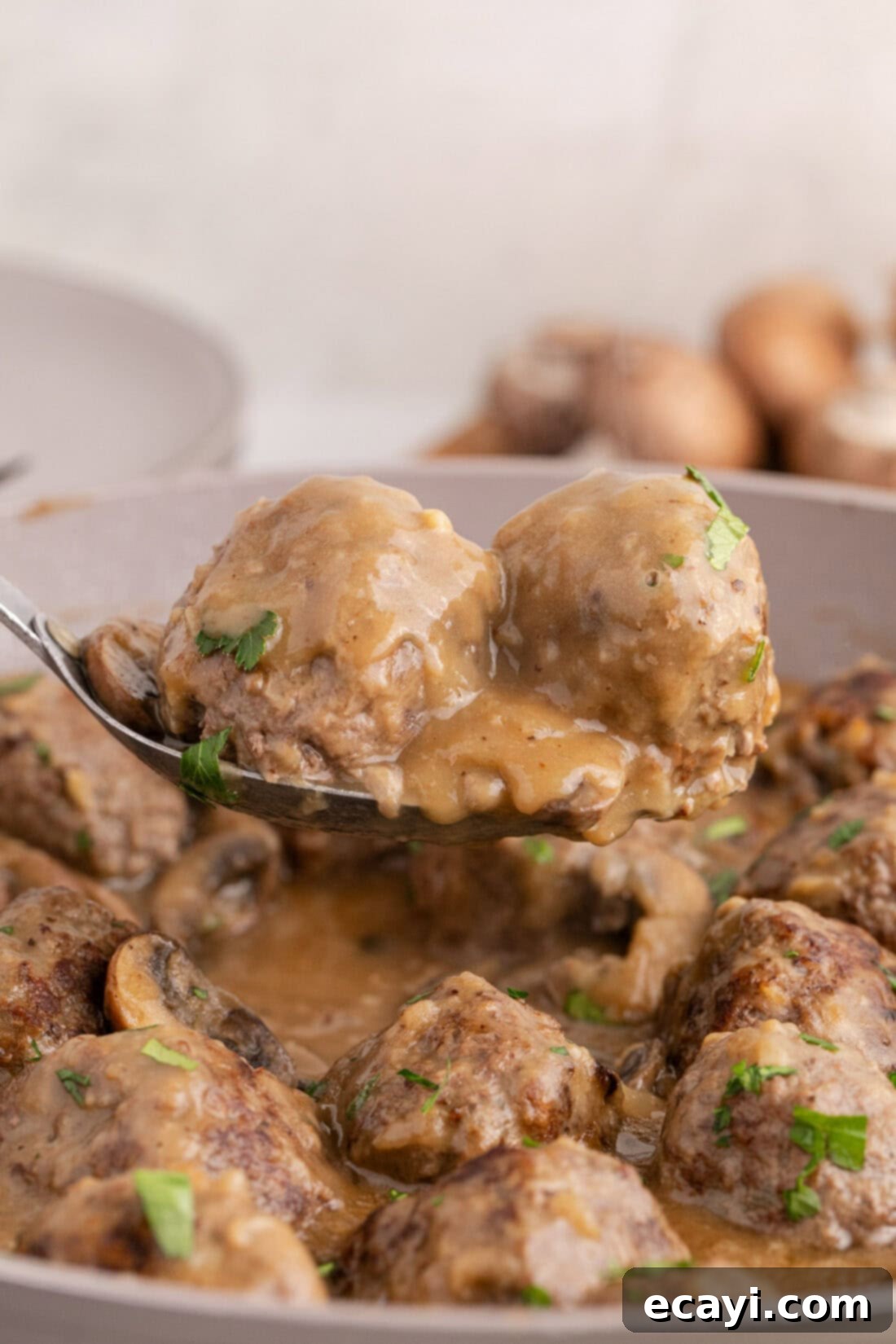 Hearty Salisbury Steak Meatballs 2 Two Salisbury Steak Meatballs on a spoon held above a skillet of Salisbury Steak Meatballs, ready to be served and enjoyed.