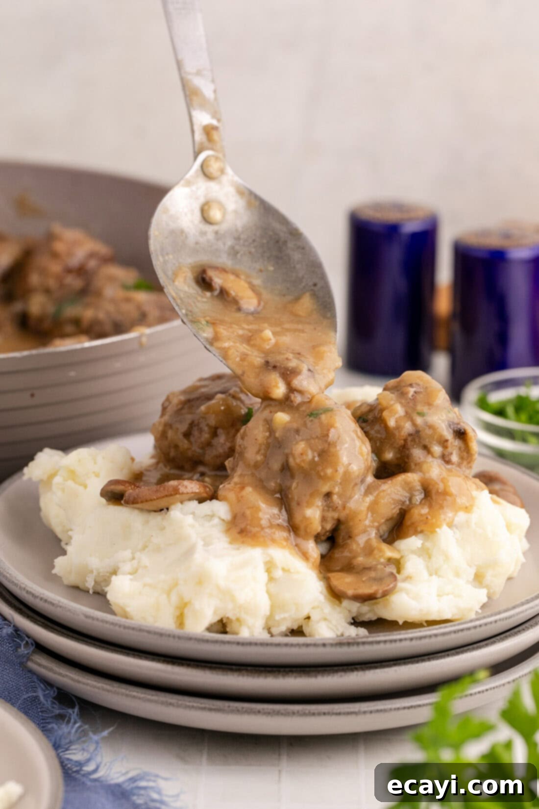 Hearty Salisbury Steak Meatballs 3 Gravy being spooned generously over Salisbury Steak Meatballs and mashed potatoes, highlighting the rich texture of the sauce.