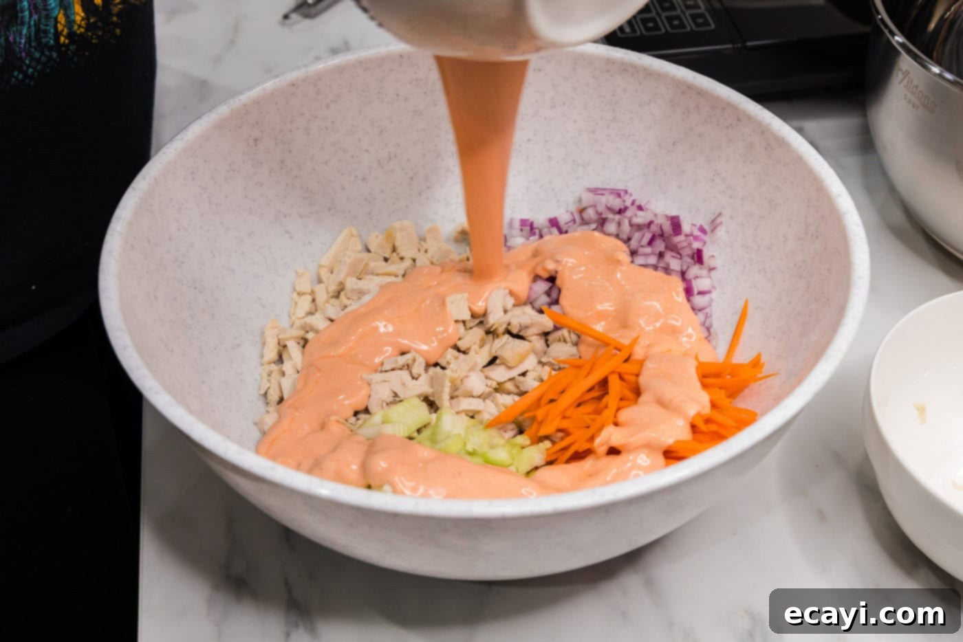 Fiery Buffalo Chicken Bowl 7 pouring buffalo sauce over the chicken and vegetable mixture in a large bowl