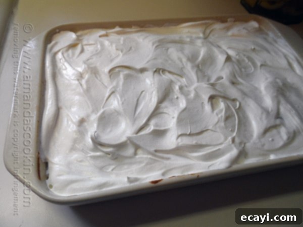 Autumn Pumpkin Pudding Poke Cake 14 A photo of fluffy whipped topping being artfully spread over the entire surface of the pumpkin pudding poke cake, completing the dessert.