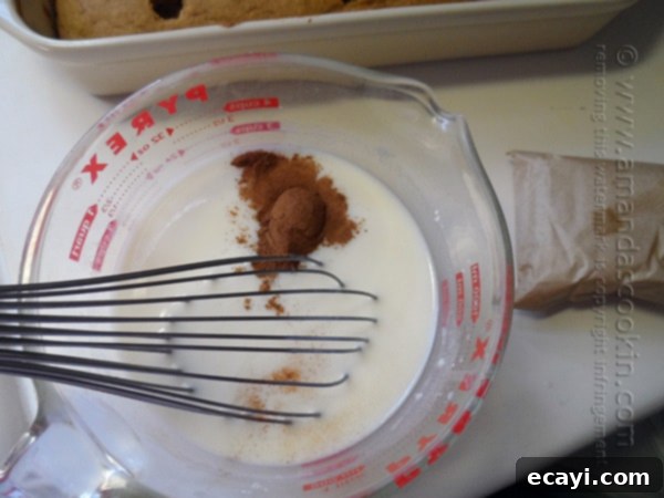 Autumn Pumpkin Pudding Poke Cake 6 A close up photo of white chocolate instant pudding mix, ground cinnamon, and milk being whisked together in a large measuring cup.