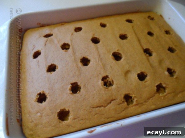Autumn Pumpkin Pudding Poke Cake 7 An overhead photo of a freshly baked pumpkin cake in a baking dish, dotted with neatly poked holes using a spoon handle.