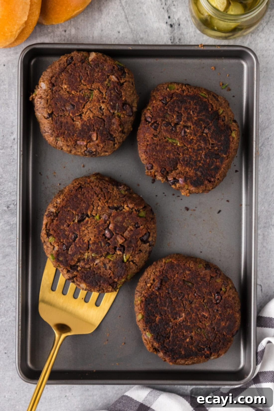 Signature Black Bean Burger 2 Four Black Bean Burger patties on a baking sheet with a spatula