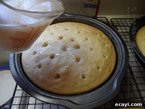 Blissful Almond Coconut Snowflake Cake 10 Cream of coconut being slowly poured over a cake layer with poked holes, allowing the liquid to soak in.