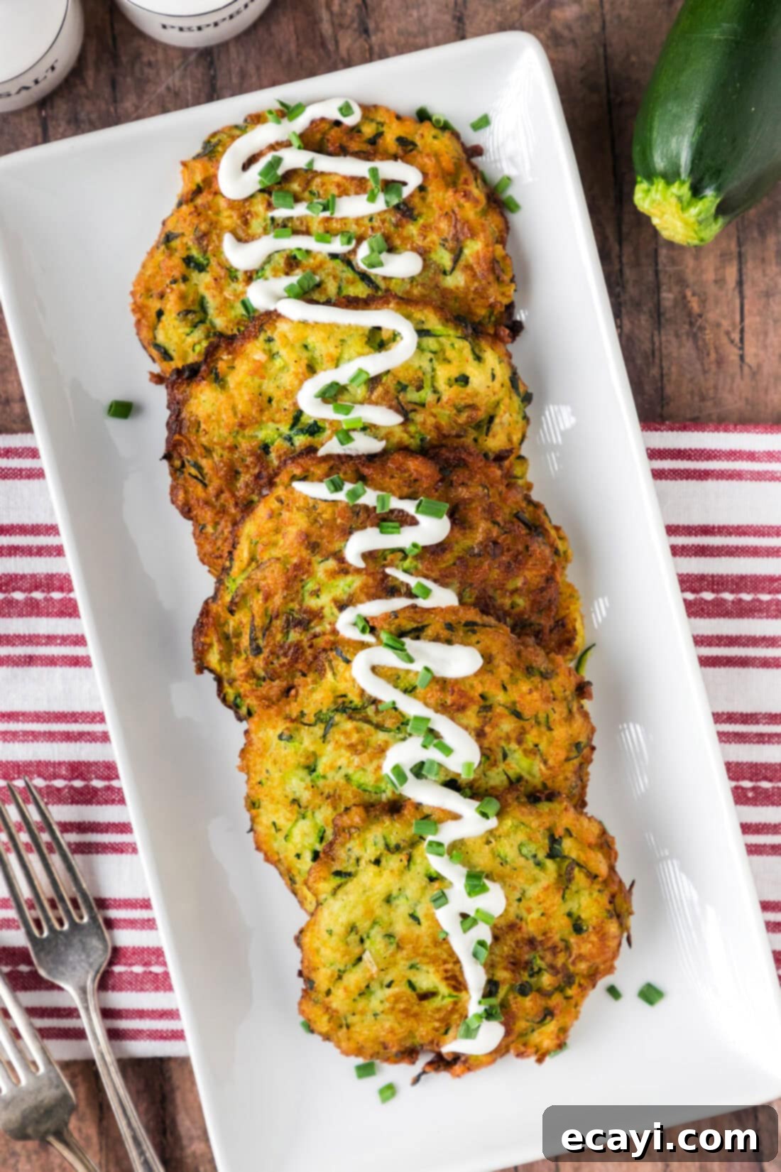Crispy Zucchini Delights 3 Zucchini Fritters on a platter with sour cream drizzled on top