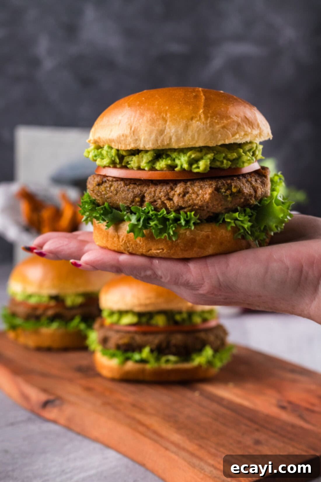Plant-Based Burgers 3 Hand holding up a Veggie Burger with two more on a platter in the background