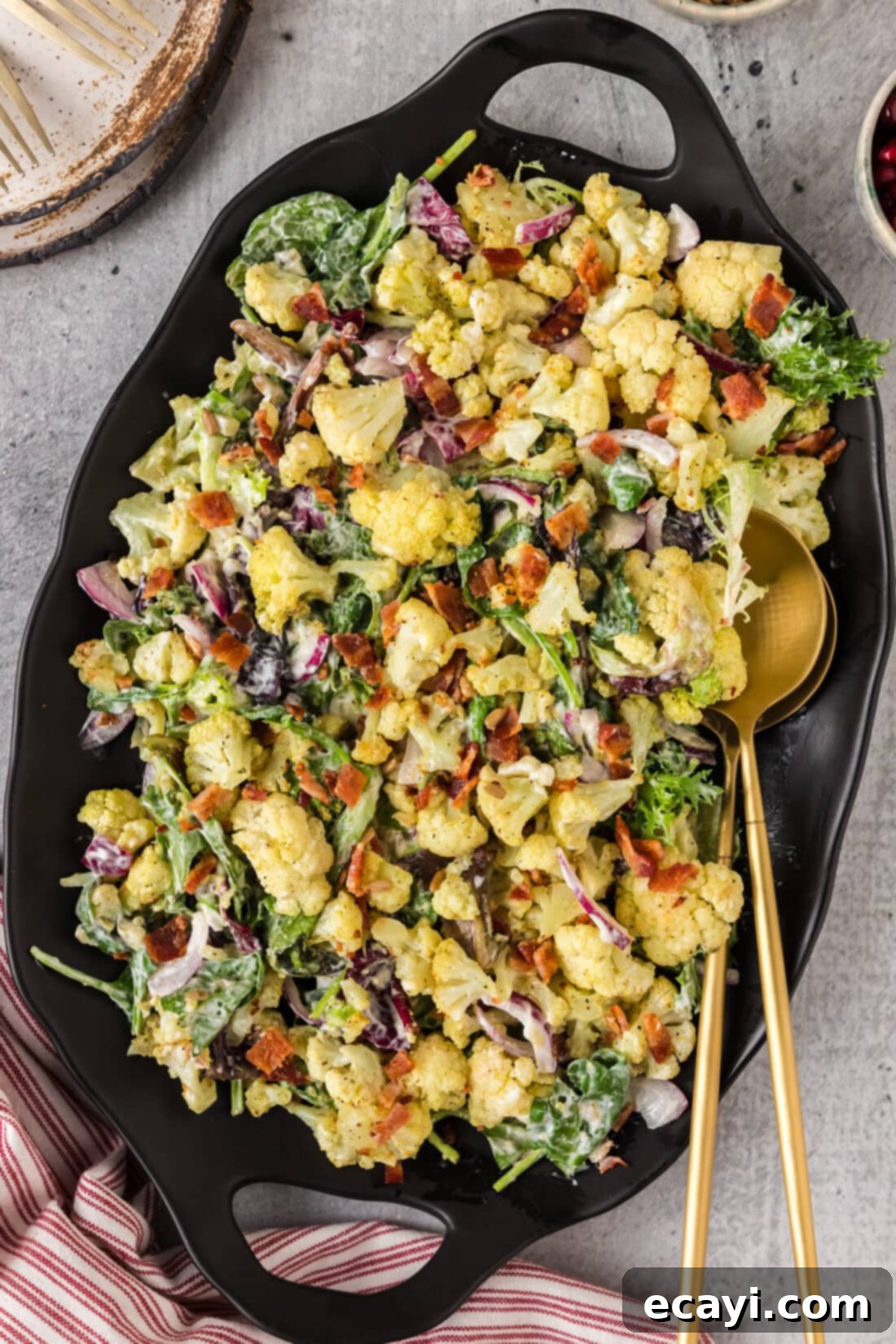 Zesty Cauliflower Medley 2 Cauliflower Salad on a black platter with two serving spoons, ready to be enjoyed at a gathering.