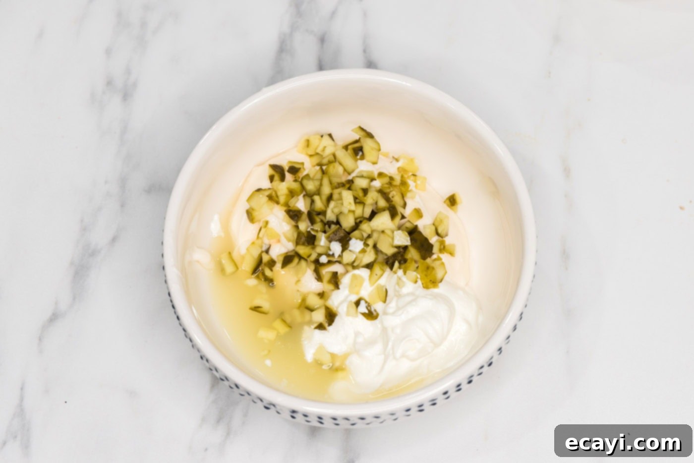 Zesty Cauliflower Medley 8 A bowl containing diced pickles, mayonnaise, sour cream, and lemon juice for the salad dressing.