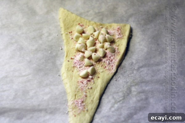 Festive White Chocolate Candy Cane Cookies 10 A close-up shot of a Pillsbury crescent dough triangle, topped generously with white chocolate chips and a sprinkling of fine candy cane powder, ready for rolling.