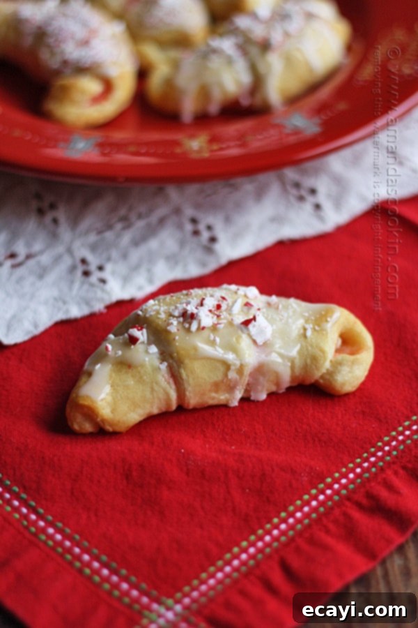 Festive White Chocolate Candy Cane Cookies 3 A close up photo of a single white chocolate candy cane crescent resting on a festive red napkin, highlighting its flaky texture and peppermint topping.
