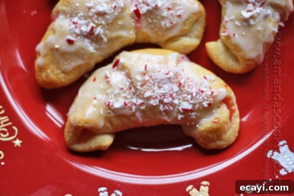 Festive White Chocolate Candy Cane Cookies 4 A beautiful close up of a white chocolate candy cane crescent on a red plate, showcasing the glazed finish and crushed candy cane sprinkles.