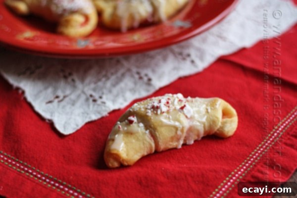 Festive White Chocolate Candy Cane Cookies 6 A detailed close up of a single white chocolate candy cane crescent, showcasing its golden-brown crust and glistening glaze with peppermint bits.