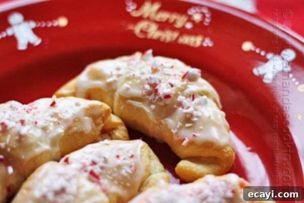 Festive White Chocolate Candy Cane Cookies 7 Another close up of a white chocolate candy cane crescent on a red plate, emphasizing the light glaze and visible peppermint pieces.