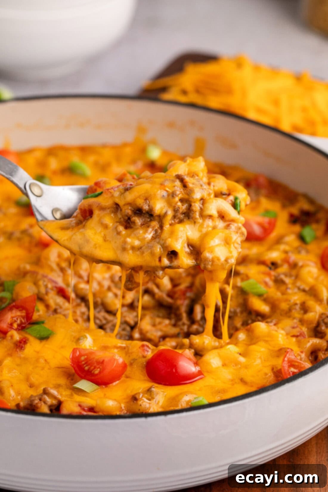 Taco Mac 'n' Cheese 2 Spoon lifting Taco Macaroni and Cheese out of a skillet, showcasing the creamy texture and rich ingredients.