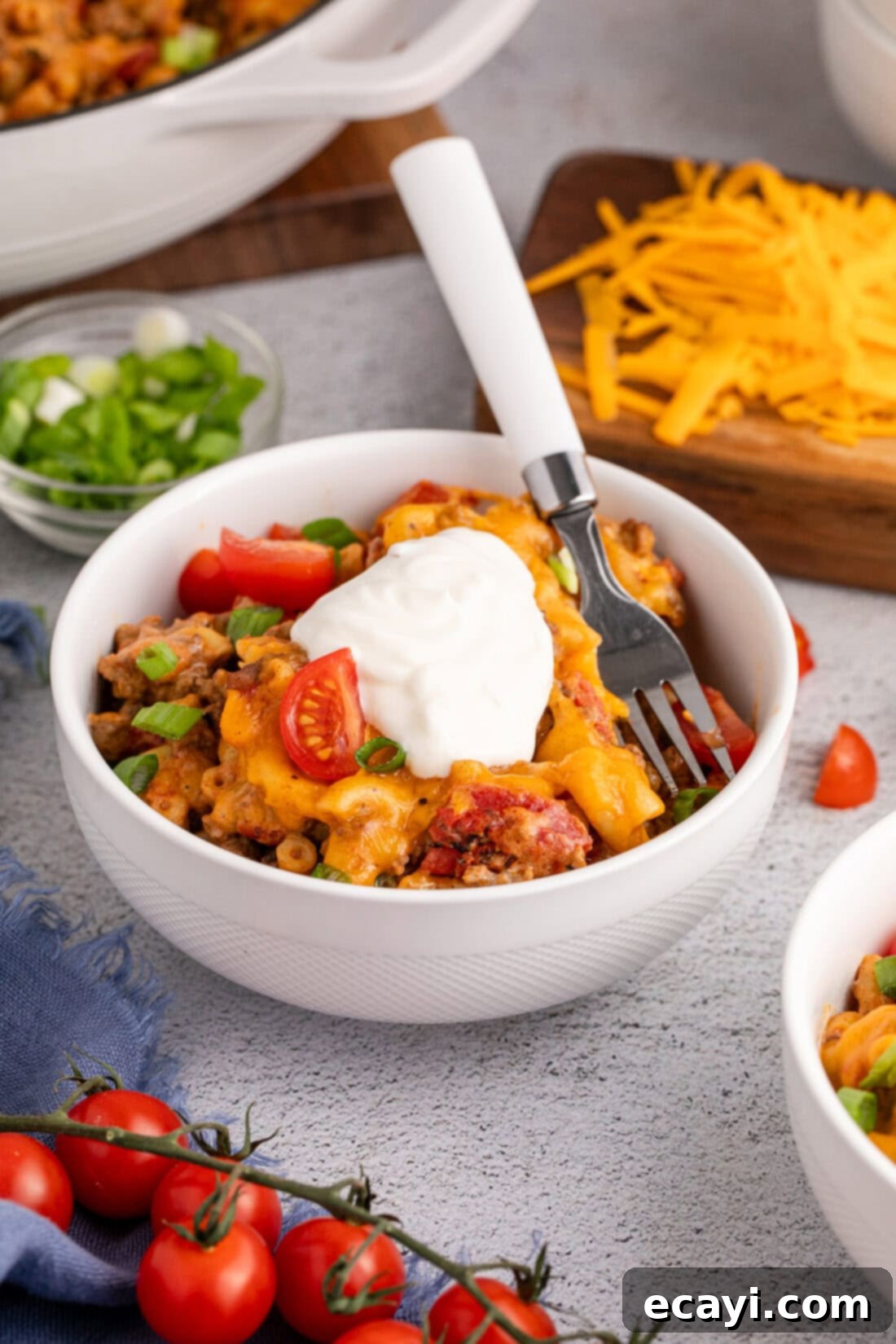 Taco Mac 'n' Cheese 12 Bowl of Taco Macaroni and Cheese topped with sour cream, green onions, and fresh diced tomatoes, ready to enjoy.