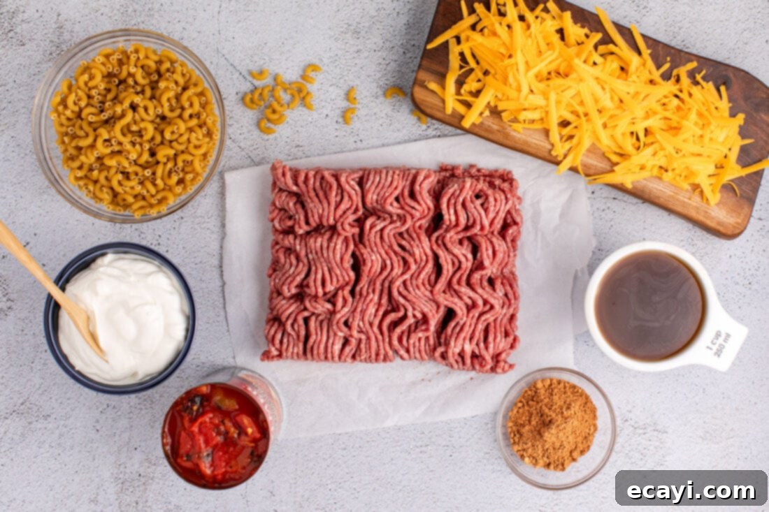 Taco Mac 'n' Cheese 4 Ingredients for Taco Macaroni and Cheese laid out on a kitchen counter, including ground beef, pasta, tomatoes, and cheese.