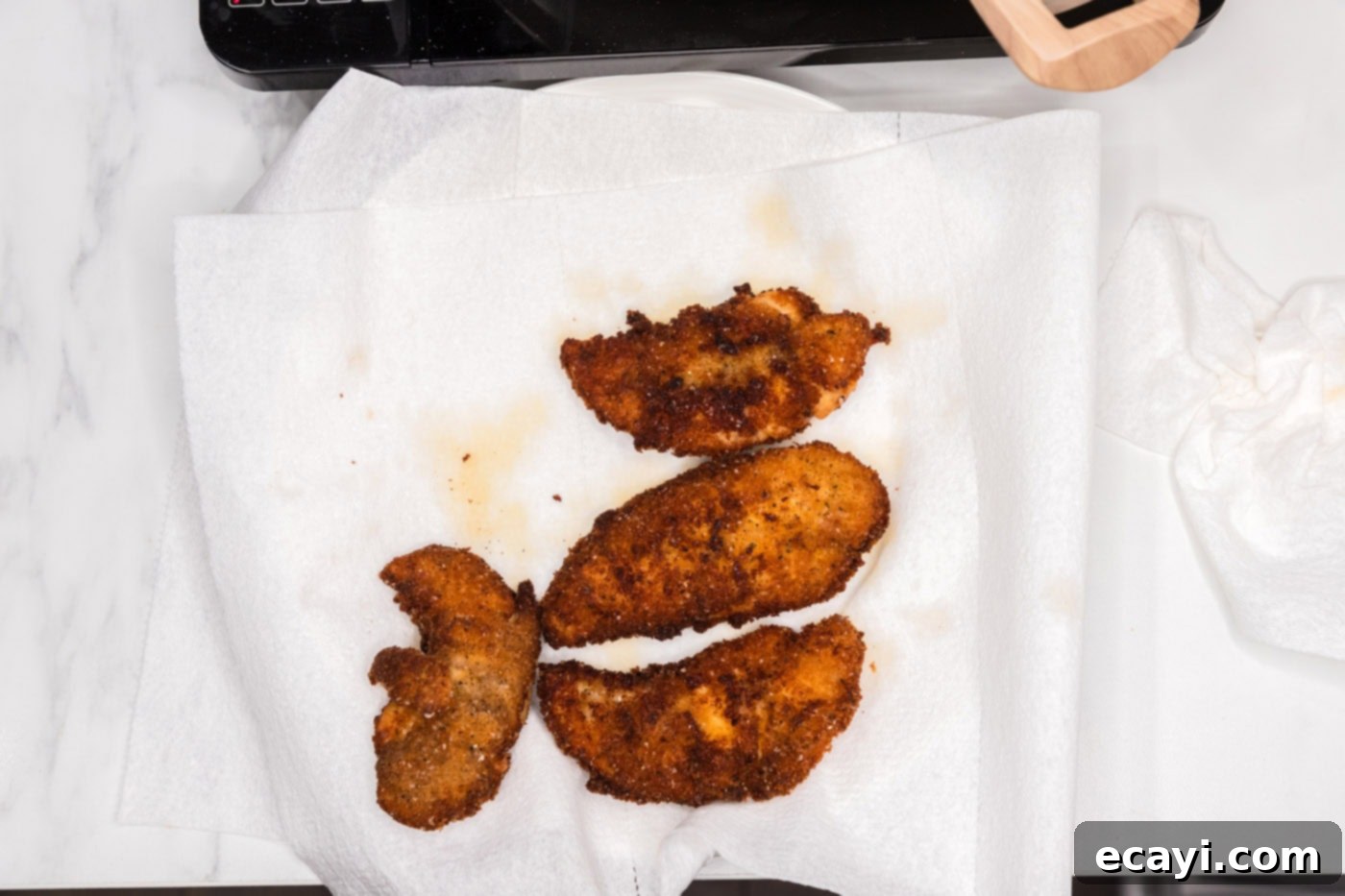 Signature Buffalo Chicken Strips 11 Crispy fried chicken tenders draining on a plate lined with paper towels after being removed from the hot oil.