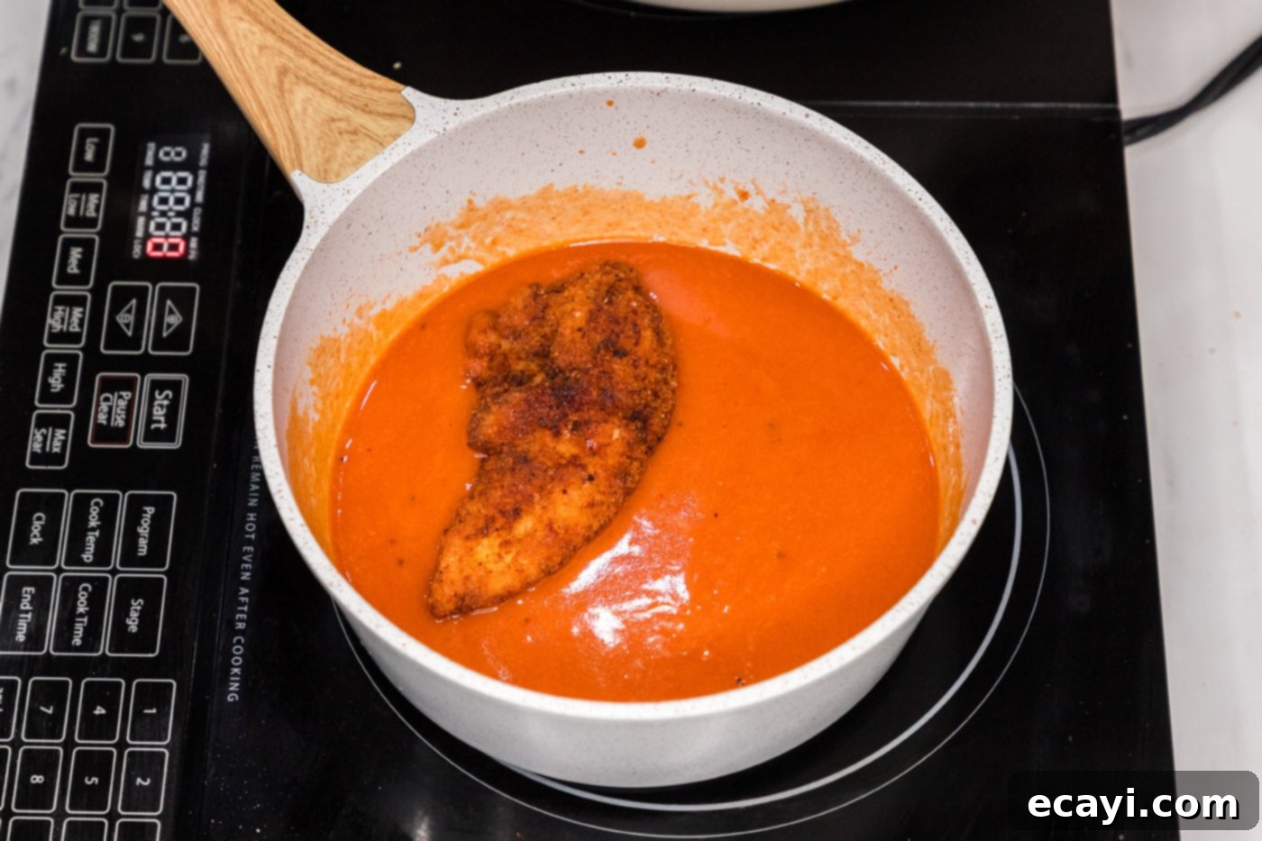 Signature Buffalo Chicken Strips 13 A fried chicken tender being dipped and coated in the homemade buffalo sauce within a pan.