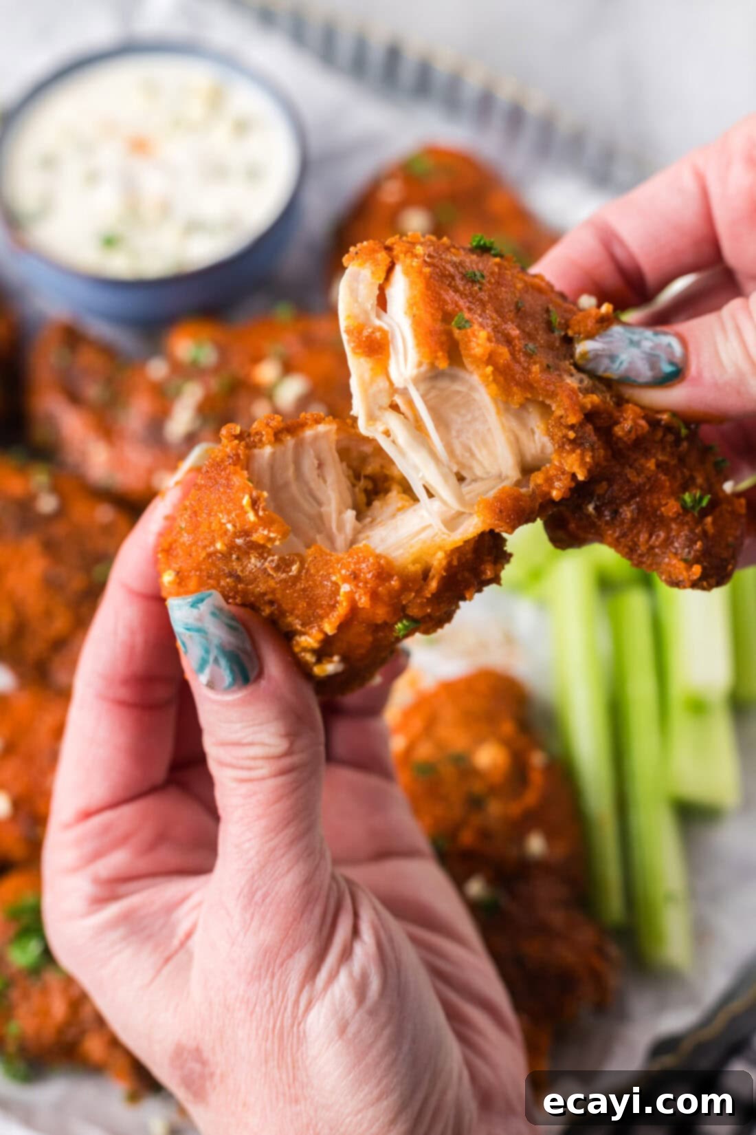 Signature Buffalo Chicken Strips 15 A Buffalo Chicken Tender broken in half, revealing the juicy white meat inside and the thick, crispy breading.
