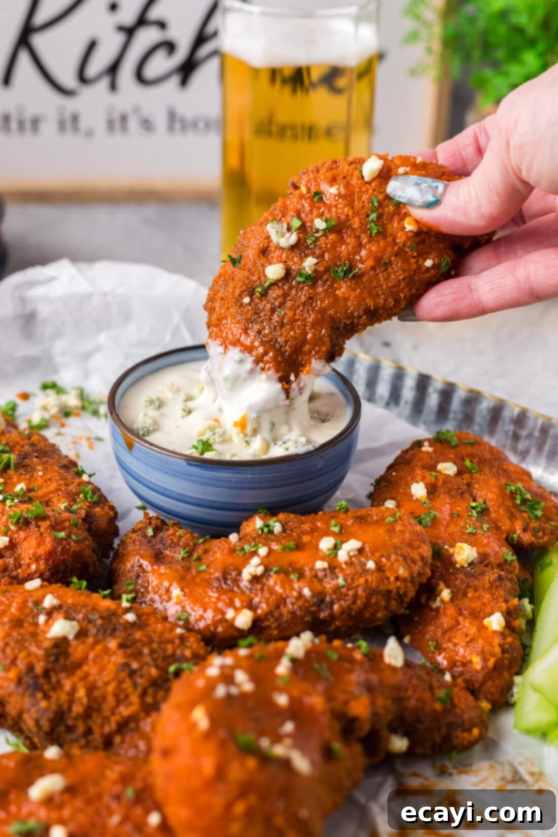 Signature Buffalo Chicken Strips 3 A golden-brown Buffalo Chicken Tender being dipped into a creamy blue cheese dressing, showcasing its crispy texture.