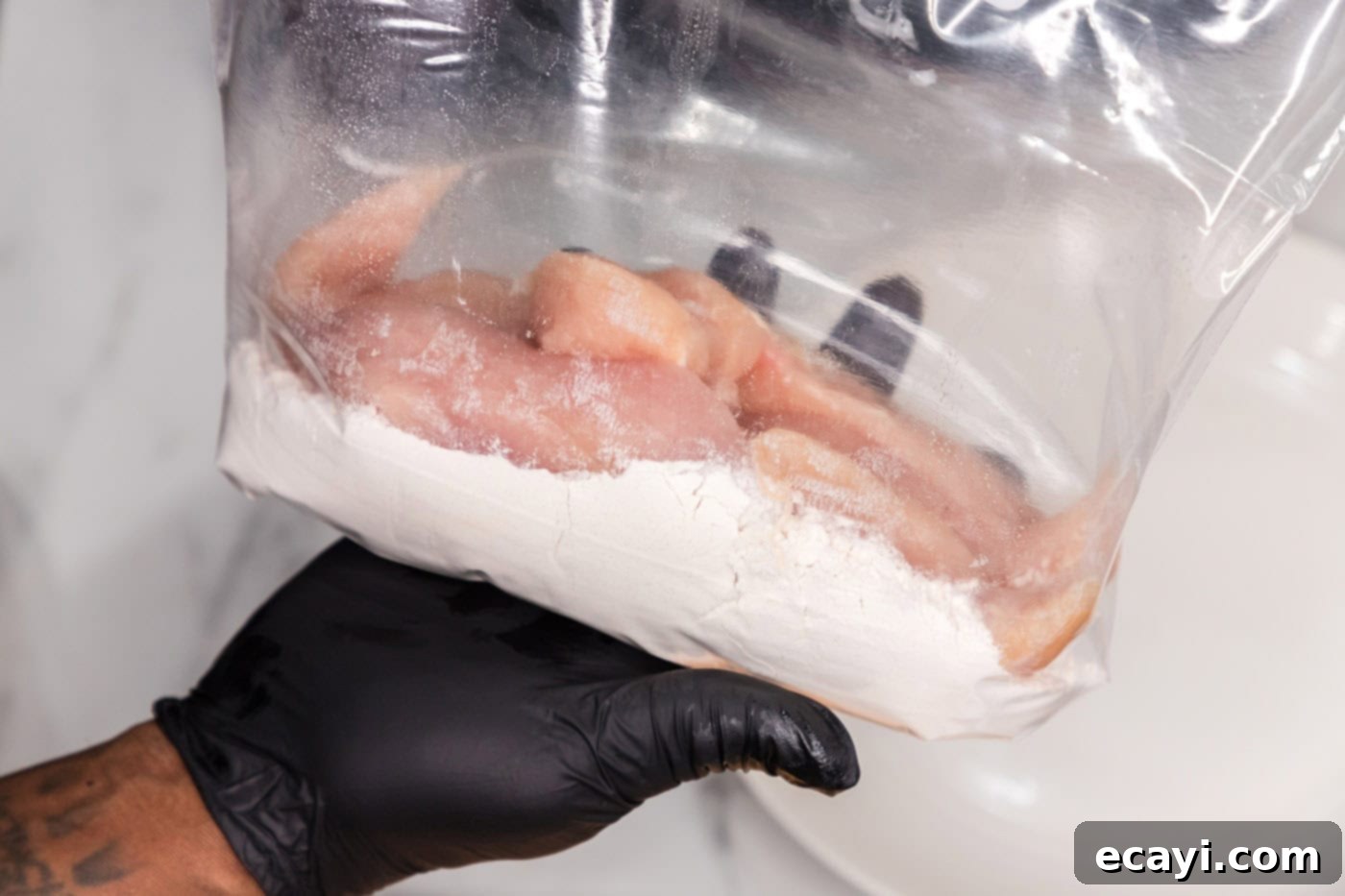 Signature Buffalo Chicken Strips 5 Chicken tenderloins being placed into a gallon-sized zipper bag with flour for coating.