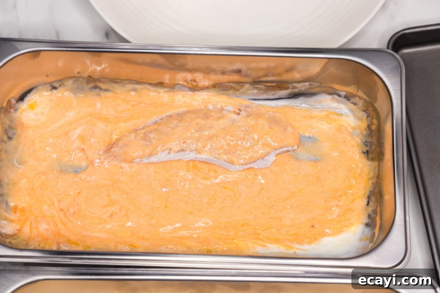 Signature Buffalo Chicken Strips 7 A floured chicken tenderloin being dipped into the buttermilk and hot sauce mixture in a breading pan.
