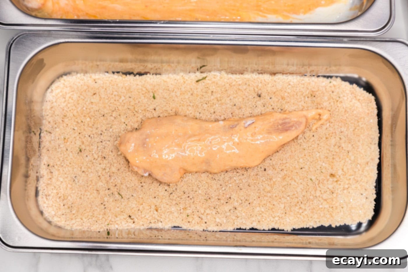 Signature Buffalo Chicken Strips 8 A chicken tenderloin coated in the buttermilk mixture being placed into the panko breadcrumb mixture.