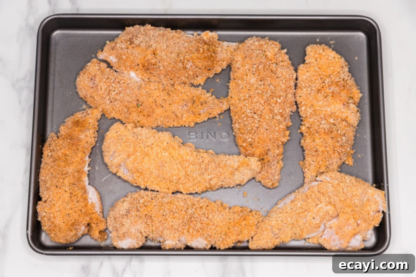 Signature Buffalo Chicken Strips 9 Several Panko-breadcrumb coated chicken tenders resting on a baking sheet, ready for frying.