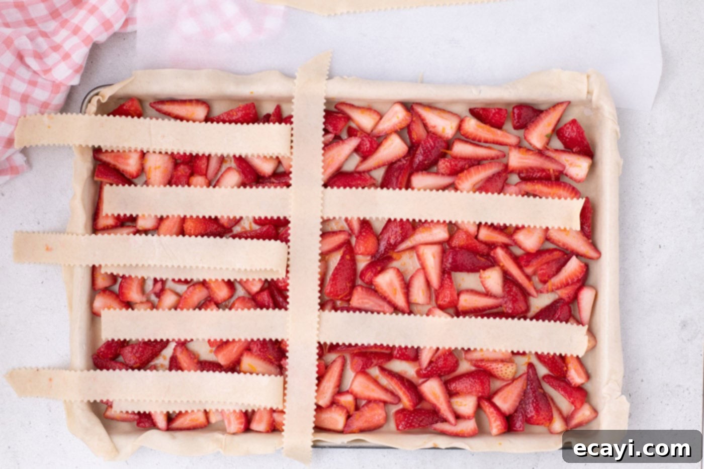 Strawberry Sheet Pan Delight 14 weaving pie crust into a lattice top over strawberries, showing initial vertical strip placement