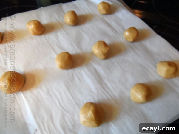 Chocolate-Stuffed Peanut Butter Perfection 7 A baking sheet covered with parchment paper holds several perfectly shaped peanut butter cookie dough balls, each with the distinctive criss-cross pattern pressed into its surface, ready for the oven.