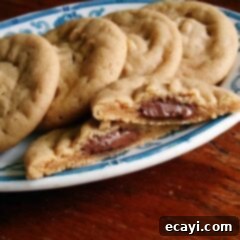 Chocolate-Stuffed Peanut Butter Perfection 10 A close-up of a Hershey drop stuffed peanut butter cookie split in half on a plate with whole cookies in the background.