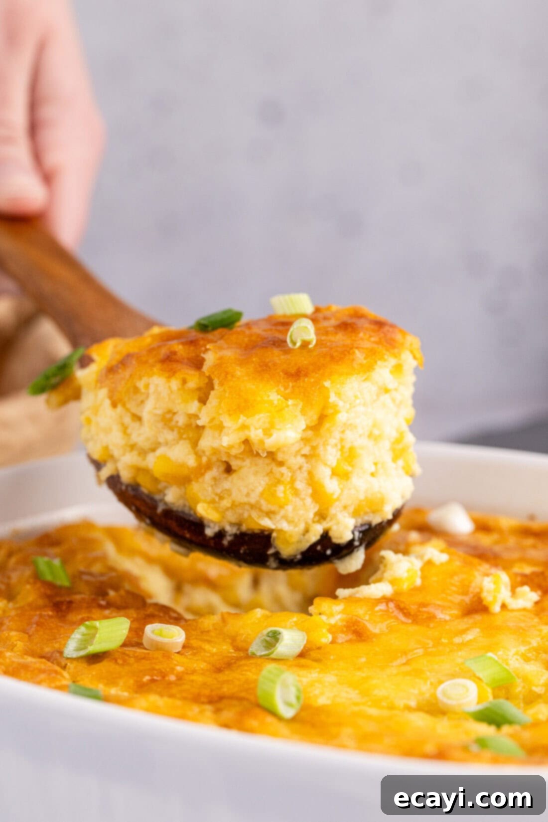 Creamy Golden Corn Bake 3 A serving spoon lifting a generous scoop of creamy Corn Pudding from a baking dish, highlighting its rich texture and golden top
