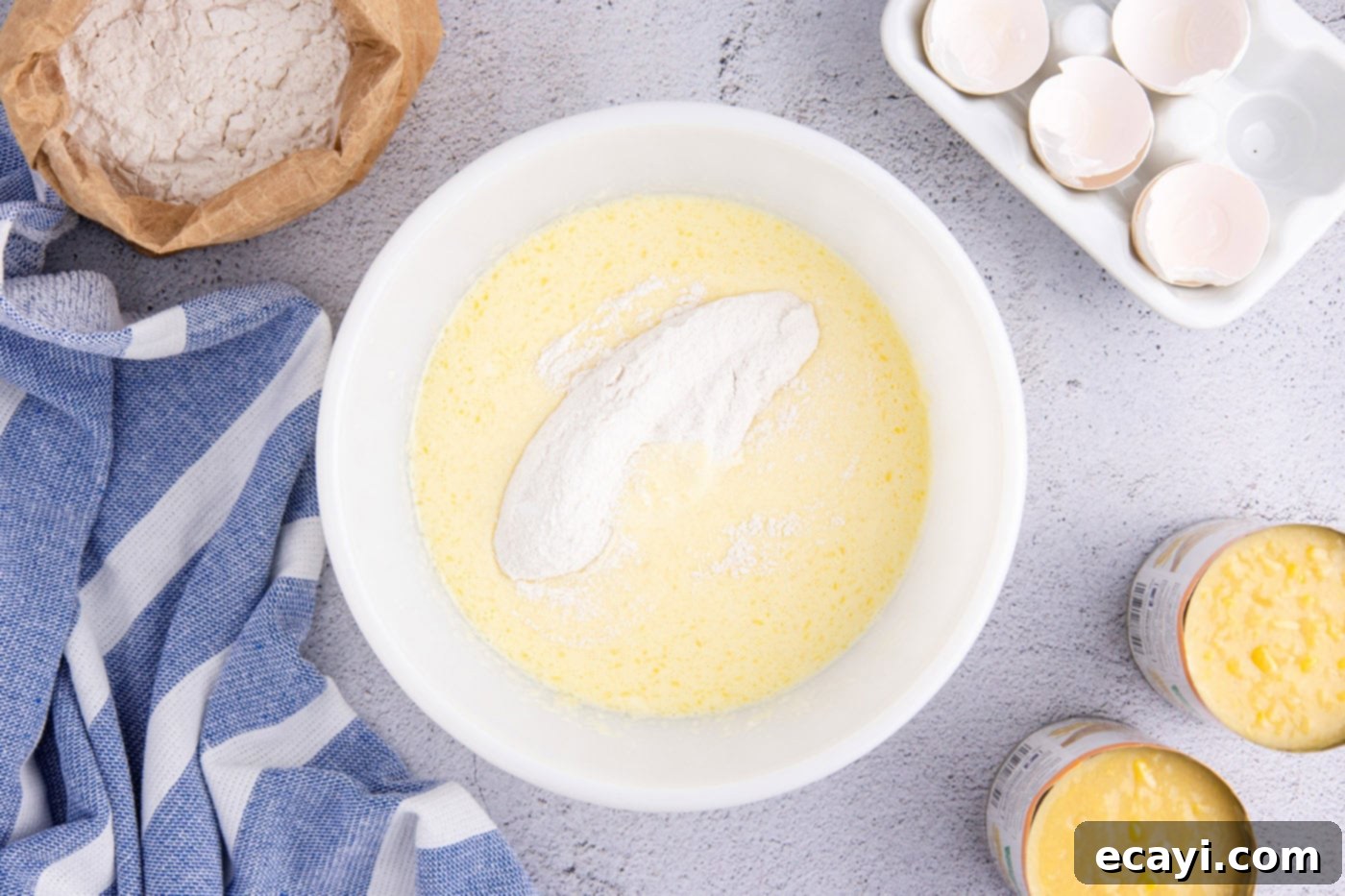 Creamy Golden Corn Bake 7 The dry ingredients (flour, sugar, baking powder, salt) being added to the wet ingredients (eggs, milk, butter, sour cream) in a large mixing bowl, for the corn pudding batter