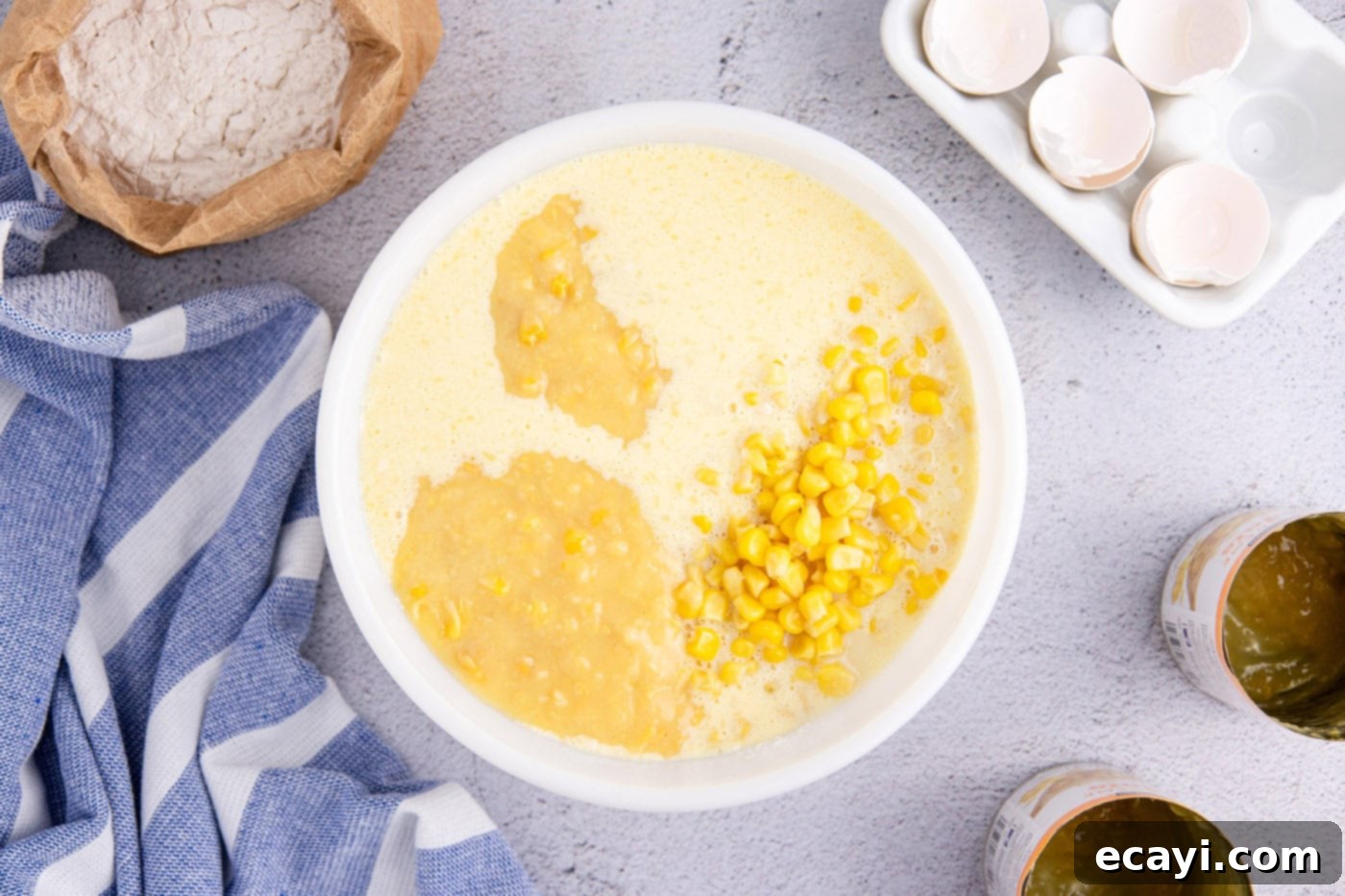 Creamy Golden Corn Bake 8 Drained whole kernel corn and cream style corn being stirred into the smooth corn pudding batter in a mixing bowl