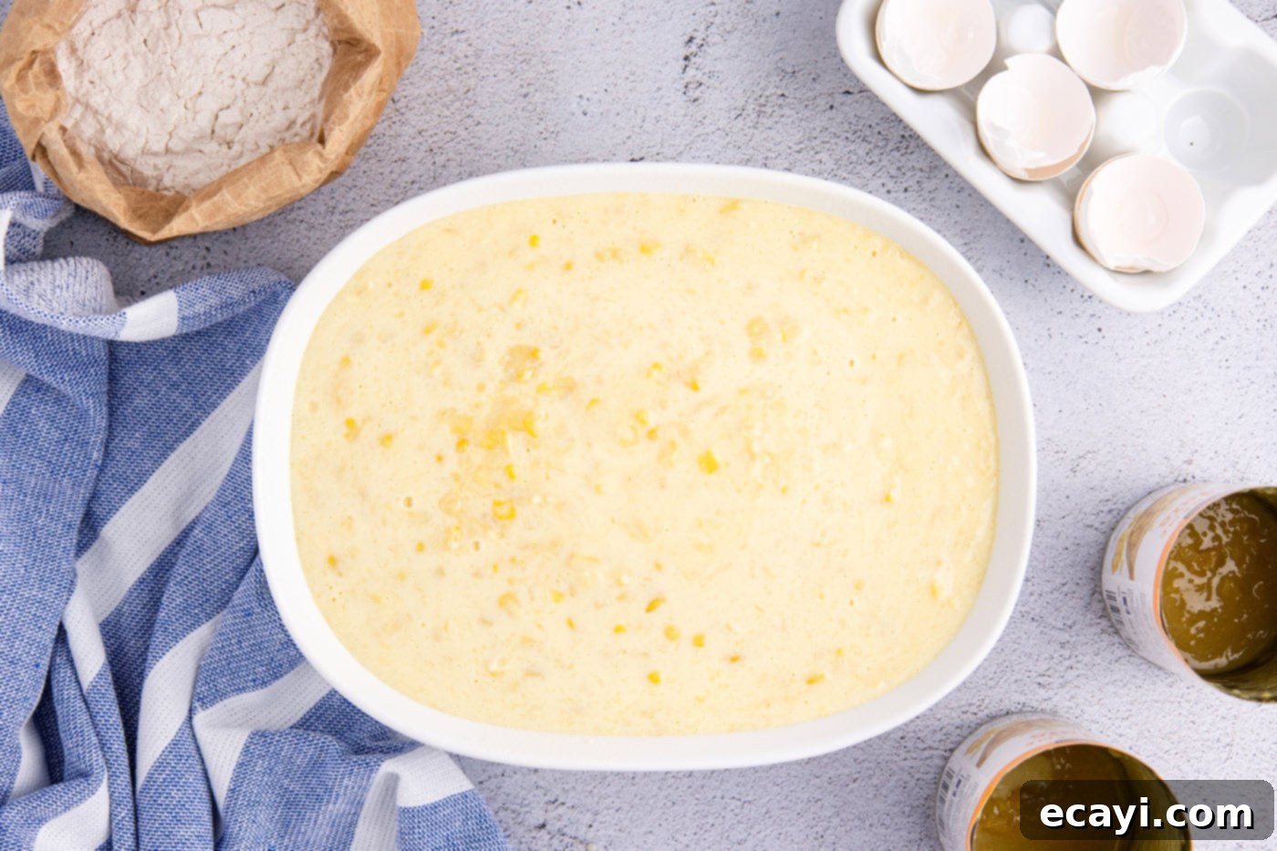Creamy Golden Corn Bake 9 An overhead shot of uncooked corn pudding batter, filled with corn kernels, poured into an oval baking dish, ready for the oven