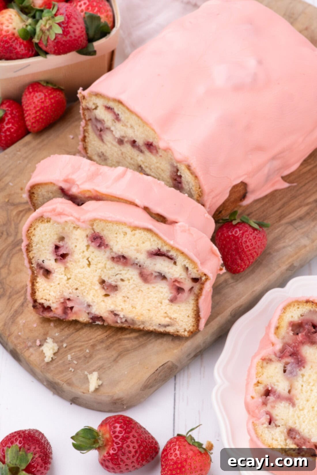 Luscious Strawberry Pound Cake 3 A whole Strawberry Pound Cake on a wooden board with two perfectly sliced pieces, showcasing the berries inside and the glaze on top.
