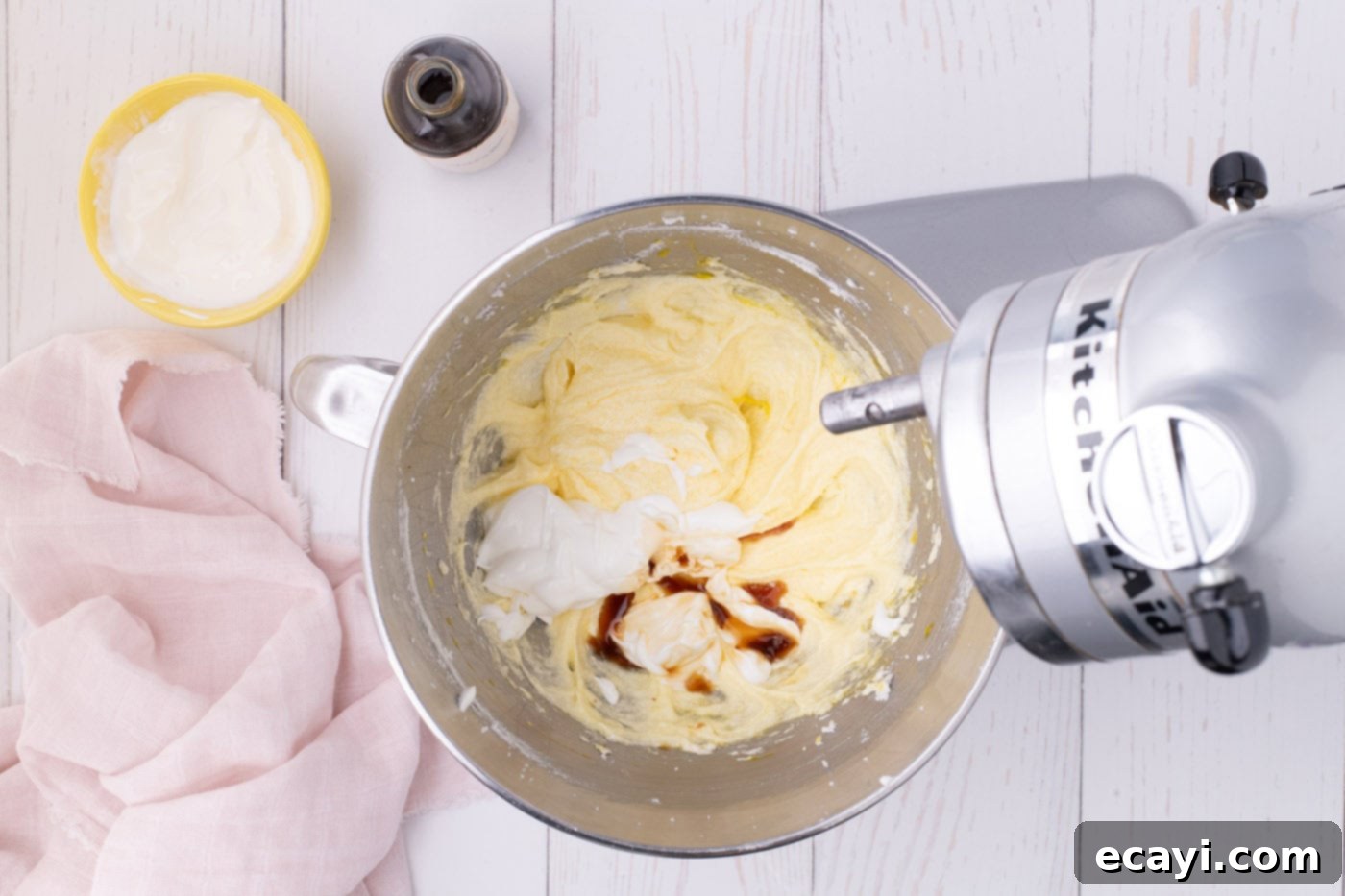 Luscious Strawberry Pound Cake 7 Vanilla extract and sour cream being added to the creamed butter, sugar, and egg mixture in a stand mixer, blending to form a smooth batter.