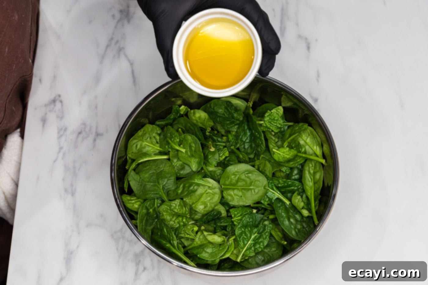 pouring olive oil over fresh spinach leaves