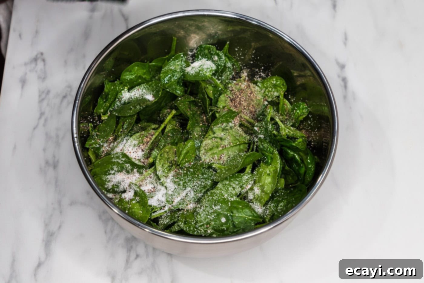 spinach leaves in a bowl with salt, pepper, and olive oil