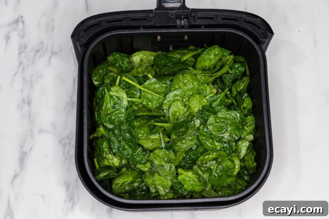 seasoned spinach leaves in an air fryer basket