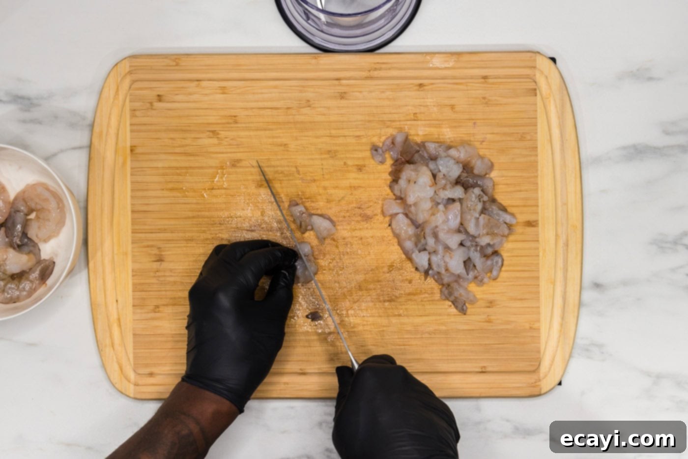 Zesty Shrimp Burger 6 A hand coarsely chopping raw shrimp on a cutting board, preparing it for the food chopper.